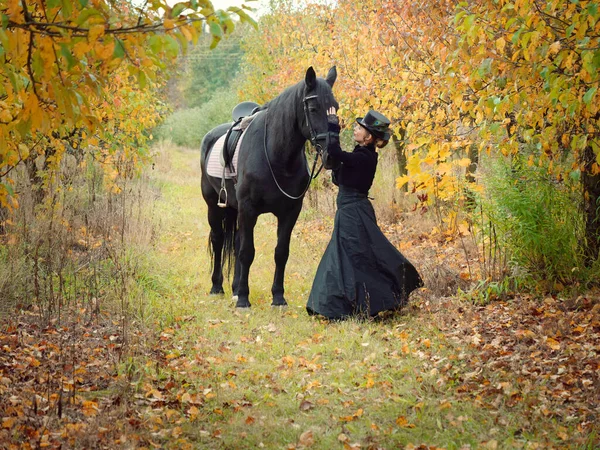 Reiterin Mädchen im schwarzen Kleid führt ein schwarzes Pferd — Stockfoto