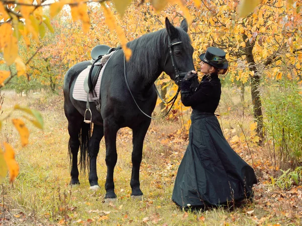 Всадница в черном платье ведет черную лошадь — стоковое фото