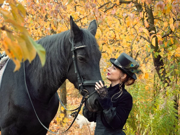 Mädchen in einem schwarzen Kleid mit einem schwarzen Pferd in Großaufnahme — Stockfoto