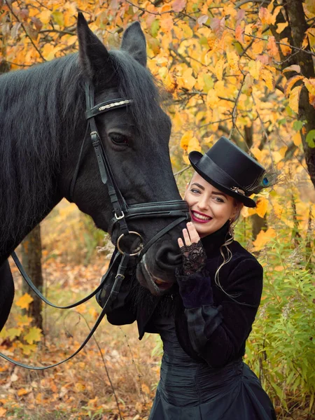 Chica en un vestido negro con un caballo negro de cerca — Foto de Stock