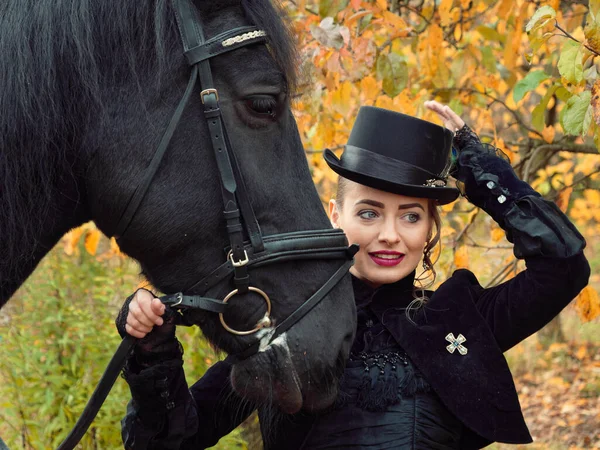 Chica en un vestido negro con un caballo negro de cerca — Foto de Stock