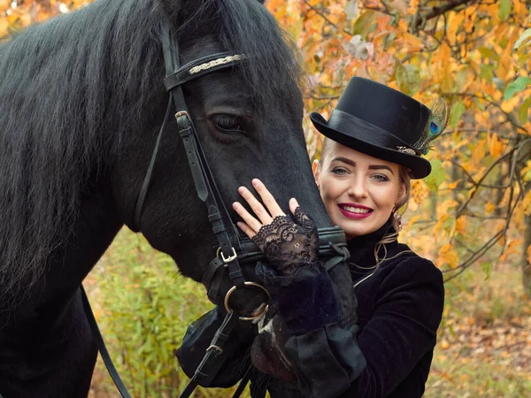 Mädchen in einem schwarzen Kleid mit einem schwarzen Pferd in Großaufnahme — Stockfoto