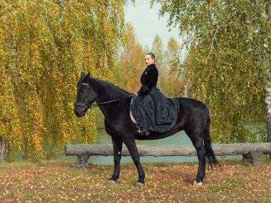 Siyah elbiseli kız siyah ata biniyor.