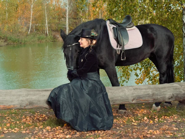 Mädchen in einem schwarzen Kleid mit einem schwarzen Pferd in Großaufnahme — Stockfoto