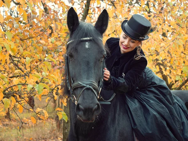 Mädchen im schwarzen Kleid reitet auf einem schwarzen Pferd — Stockfoto