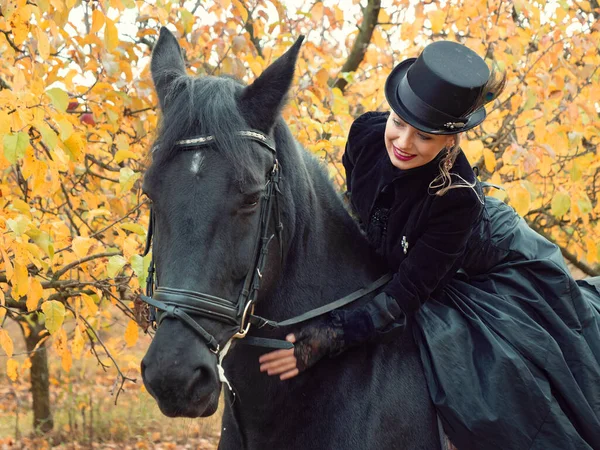 Mädchen im schwarzen Kleid reitet auf einem schwarzen Pferd — Stockfoto