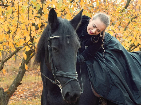 Girl in a black dress riding a black horse — Stock Photo, Image