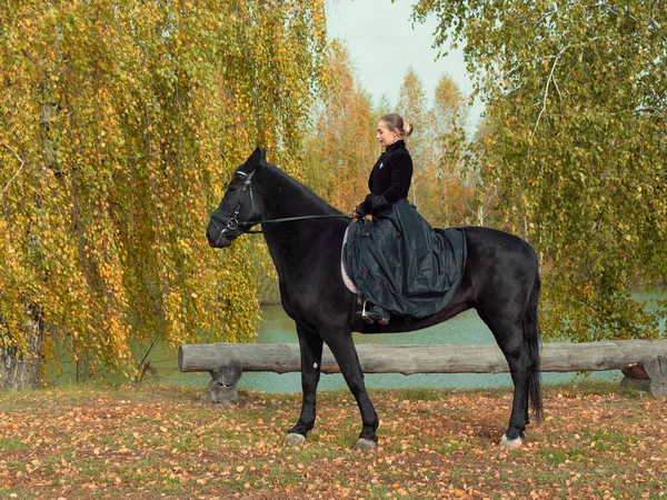 Girl in a black dress riding a black horse — Stock Photo, Image