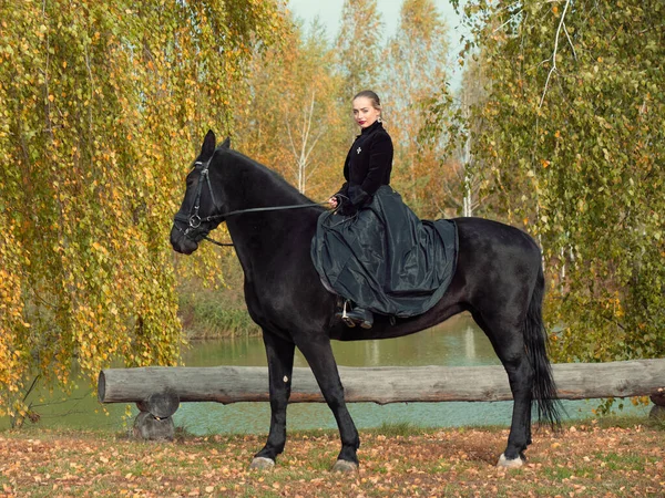 Ragazza in un abito nero cavalcando un cavallo nero — Foto Stock