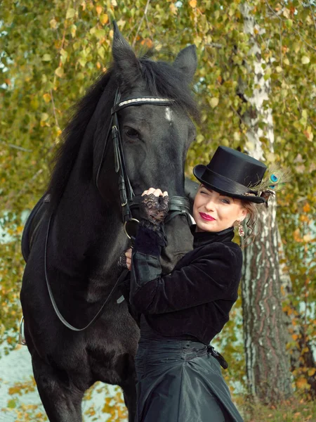 Menina em um vestido preto com um cavalo preto close-up — Fotografia de Stock