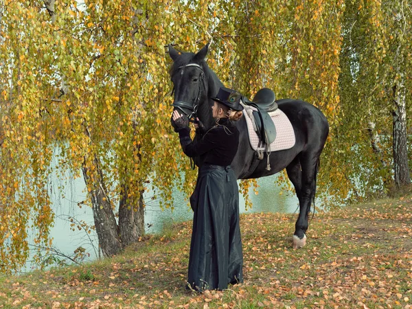 Девушка в черном платье с черной лошадью крупным планом — стоковое фото