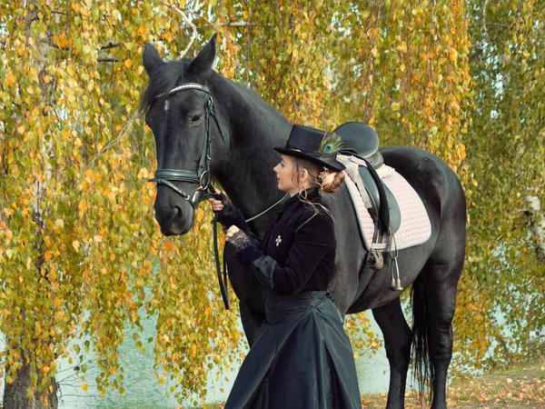 Menina em um vestido preto com um cavalo preto close-up — Fotografia de Stock