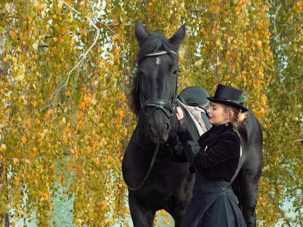 Mädchen in einem schwarzen Kleid mit einem schwarzen Pferd in Großaufnahme — Stockfoto