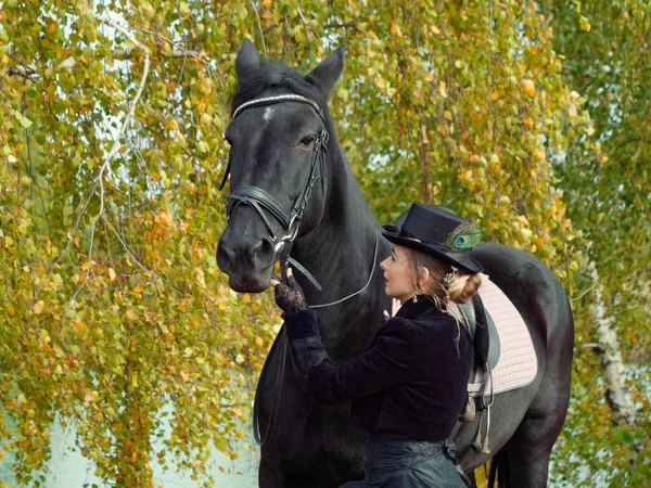 Mädchen in einem schwarzen Kleid mit einem schwarzen Pferd in Großaufnahme — Stockfoto