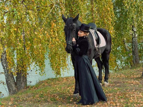 Menina em um vestido preto com um cavalo preto close-up — Fotografia de Stock