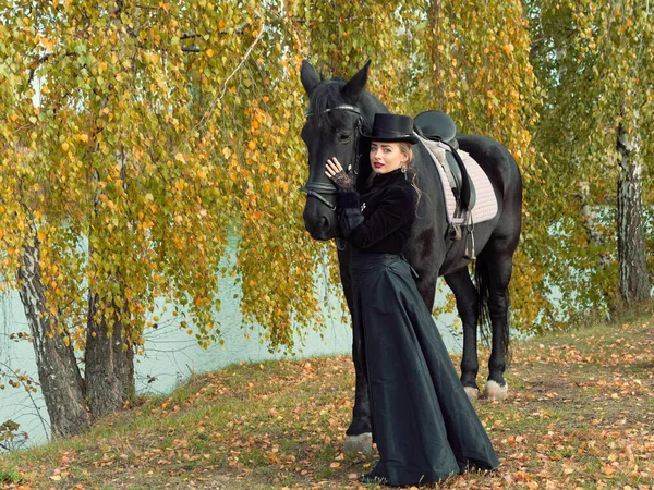 Девушка в черном платье с черной лошадью крупным планом — стоковое фото