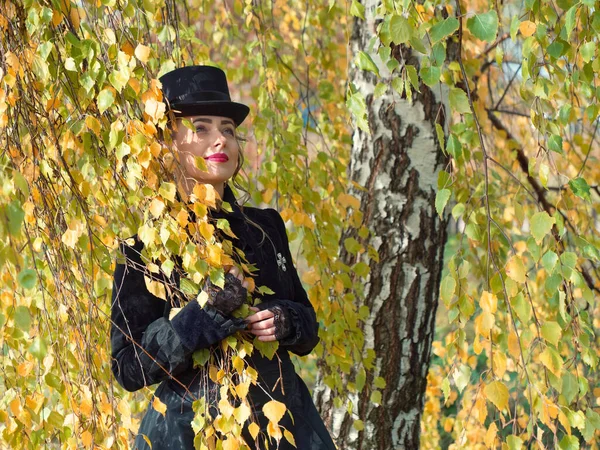 Mädchen im schwarzen Kleid in den Birkenzweigen im Herbst — Stockfoto