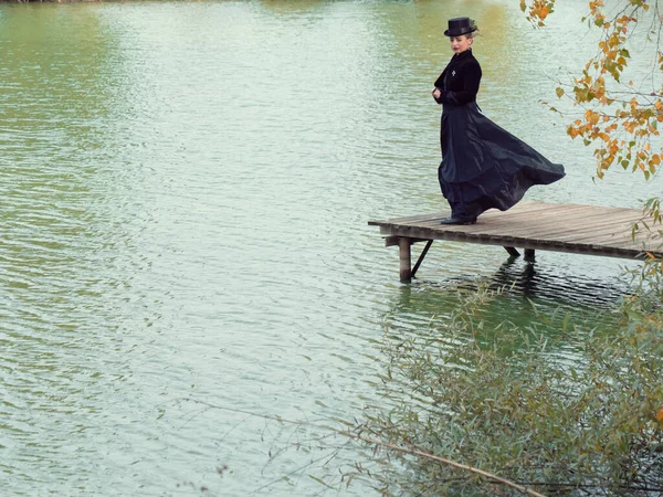 Mädchen in einem schwarzen Kleid auf einem Hintergrund aus Wasser im Herbst — Stockfoto