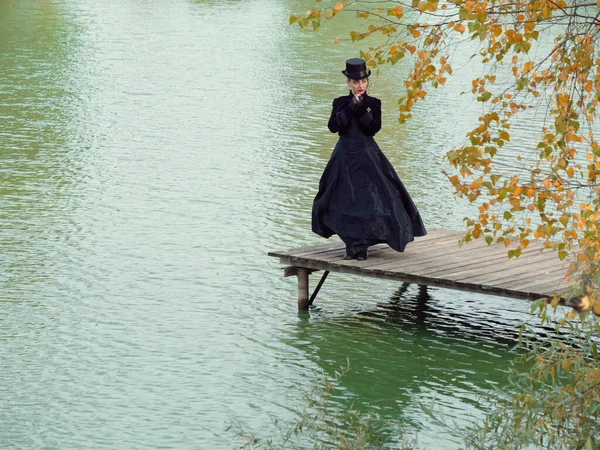 Niña en un vestido negro sobre un fondo de agua en otoño — Foto de Stock