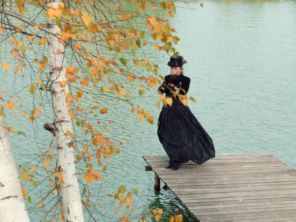 Dívka v černých šatech na pozadí vody na podzim — Stock fotografie
