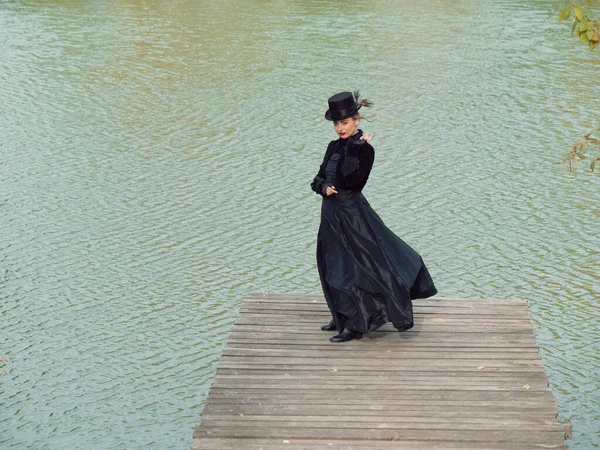 Mädchen in einem schwarzen Kleid auf einem Hintergrund aus Wasser im Herbst — Stockfoto