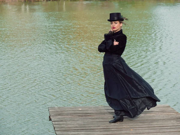 Niña en un vestido negro sobre un fondo de agua en otoño — Foto de Stock