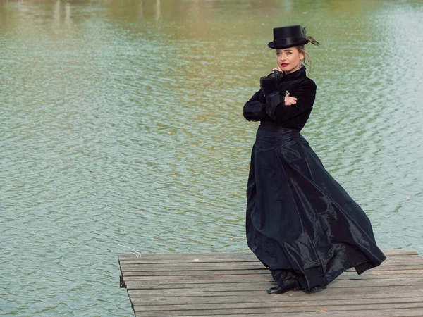 Niña en un vestido negro sobre un fondo de agua en otoño — Foto de Stock