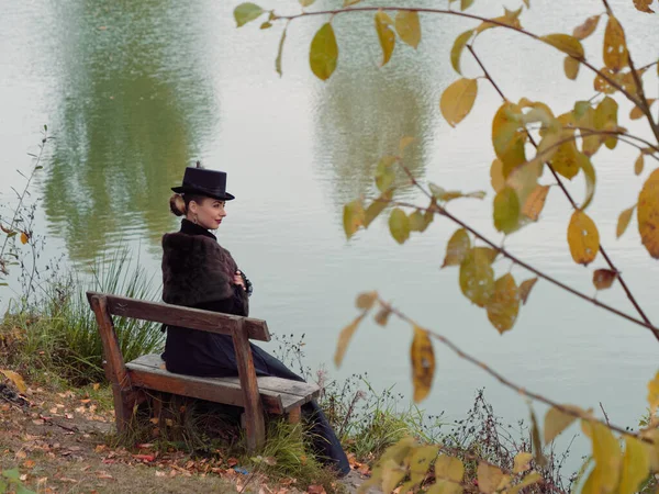 Mädchen in einem schwarzen Kleid auf einem Hintergrund aus Wasser im Herbst — Stockfoto