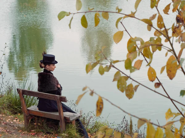 Mädchen in einem schwarzen Kleid auf einem Hintergrund aus Wasser im Herbst — Stockfoto