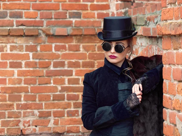 Menina em um vestido preto em um fundo de uma parede de tijolo no outono — Fotografia de Stock