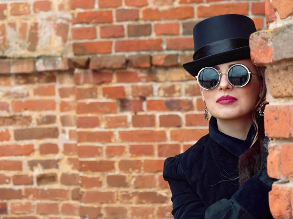 Menina em um vestido preto em um fundo de uma parede de tijolo no outono — Fotografia de Stock