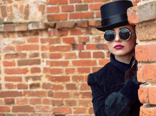 Menina em um vestido preto em um fundo de uma parede de tijolo no outono — Fotografia de Stock