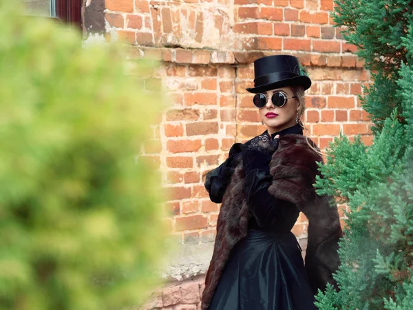 Menina em um vestido preto em um fundo de uma parede de tijolo no outono — Fotografia de Stock