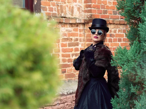 Menina em um vestido preto em um fundo de uma parede de tijolo no outono — Fotografia de Stock