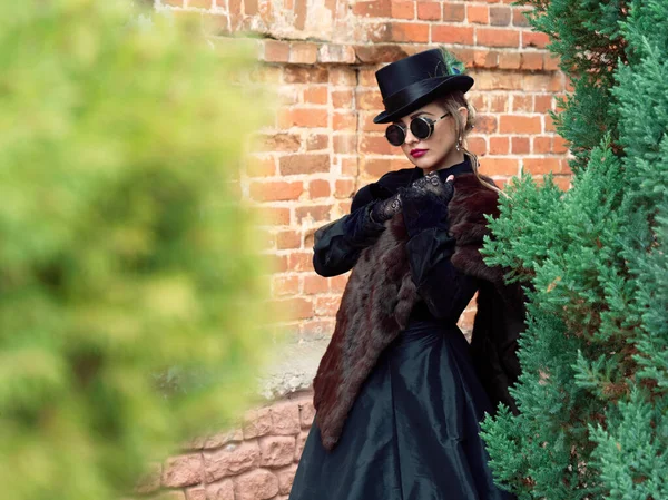 Menina em um vestido preto em um fundo de uma parede de tijolo no outono — Fotografia de Stock