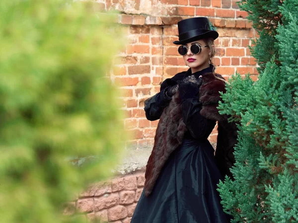 Menina em um vestido preto em um fundo de uma parede de tijolo no outono — Fotografia de Stock