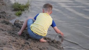Çocuk sahilin kenarında kumla oynuyor.