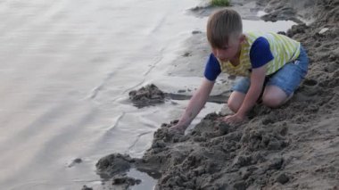 Çocuk sahilin kenarında kumla oynuyor.