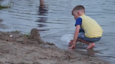 Çocuk sahilin kenarında kumla oynuyor.
