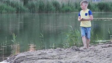 Çocuk sahilin kenarında kumla oynuyor.