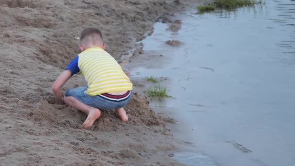 少年は海の近くのビーチで砂と遊ぶ — ストック動画