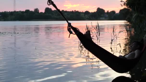 Barn svingar i en hängmatta över sjön vatten — Stockvideo
