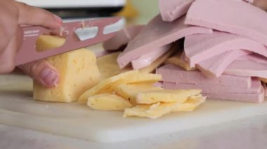 Genç, peynir ve sosisi bıçakla kesiyor.