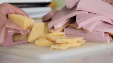 Genç, peynir ve sosisi bıçakla kesiyor.