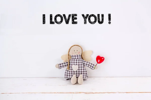 Little angel doll sitting with a balloon red heart and an I love you text