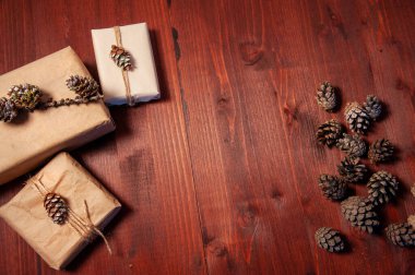 Tahta bir yüzey üzerinde el yapımı karton kutular, köknar kozalaklarıyla süslenmiş. Kutuların arasında kuru koniler var. Üst Manzara. Boşluğu kopyala