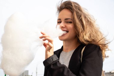 Genç ve güzel manken dışarıda gezerken büyük pamuk helva yiyor. O mutlu ve eğleniyor. Bu resim kolaylığı, hafifliği, özgürlüğü ve mutluluğu gösteriyor..