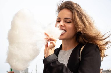 Güzel model dışarıda gezerken büyük pamuk helva yiyor. O mutlu ve eğleniyor. Bu resim kolaylığı, hafifliği, özgürlüğü ve mutluluğu gösteriyor..