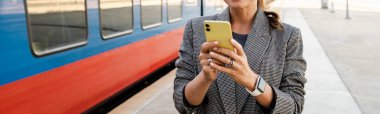 Woman checking smartphone while waiting train on railroad platform station