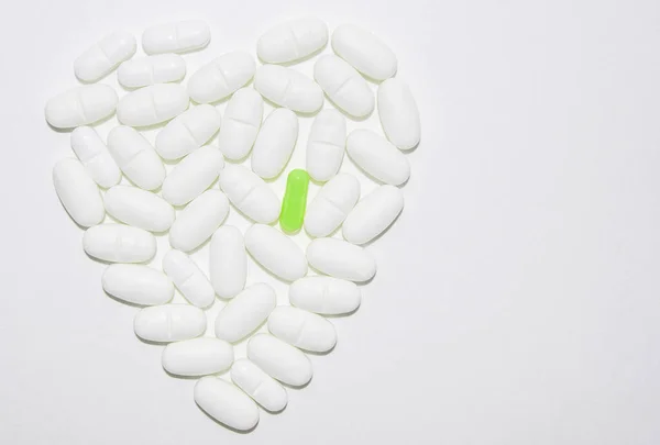 Vita piller av medicin i form av hjärta på en vit bakgrund med en grön tablett, farmaceutiskt koncept, kopiera utrymme — Stockfoto